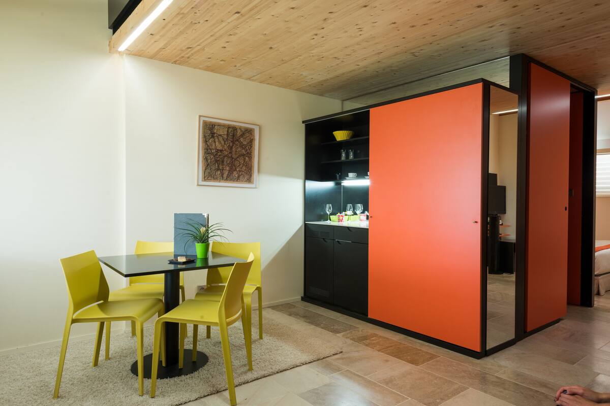 A dining area with a table and chairs, a plant, and a kitchen area with cabinets and a refrigerator.