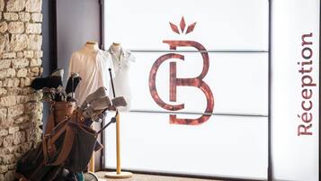 Un área de recepción con pared de piedra, un maniquí con camisa blanca y un carrito de equipaje.