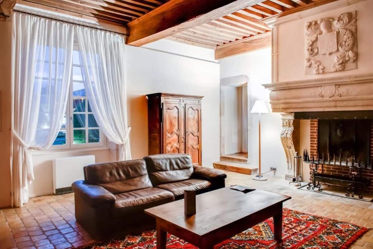 A living room with a leather sofa, a wooden coffee table, a patterned rug, a fireplace, and a large window with curtains.