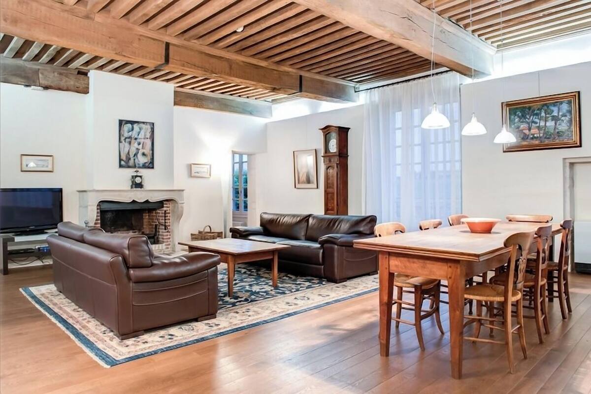 A spacious living room with a fireplace, leather sofa, wooden dining table, and a television.