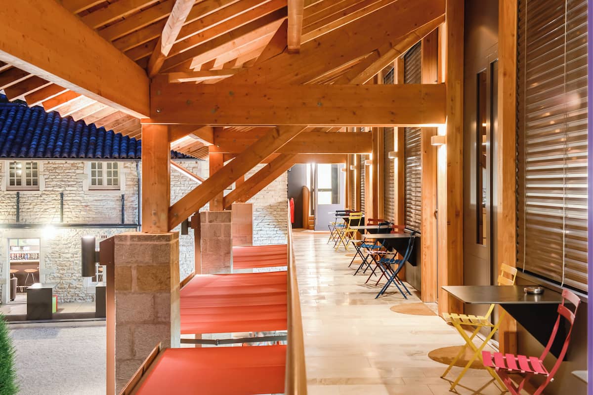 A covered outdoor area with wooden beams, a stone wall, and a staircase leading to an upper level.