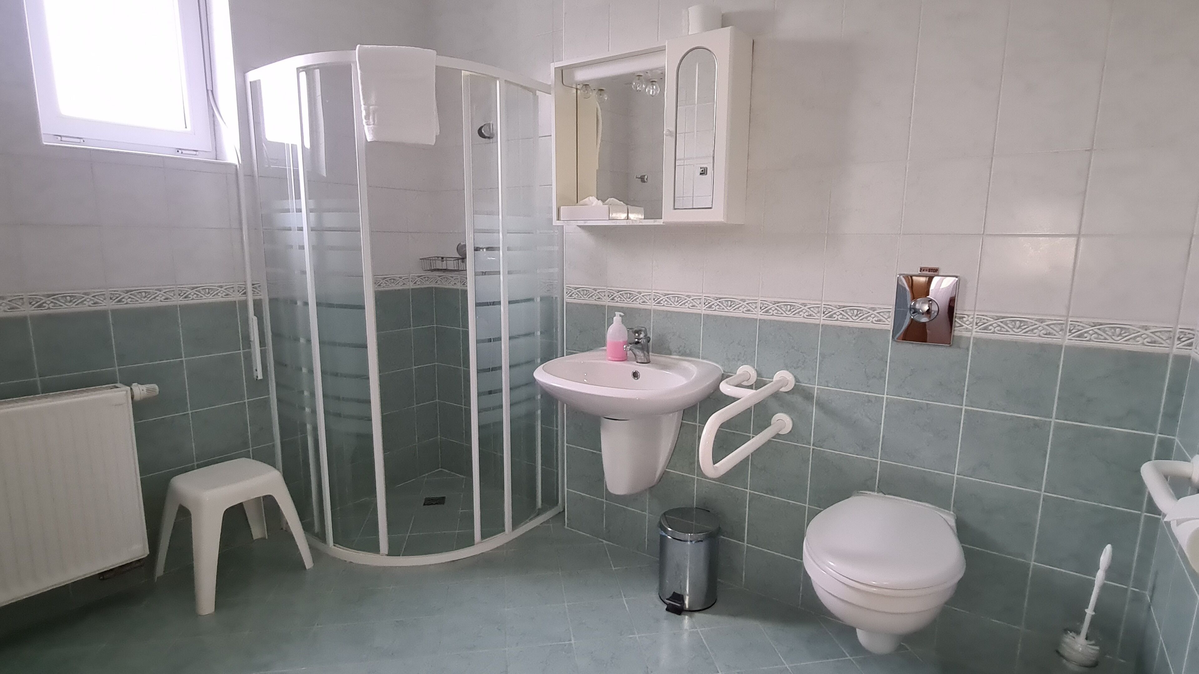 Et badeværelse med brusebad, håndvask, toilet og en lille skammel.