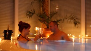 Una coppia in vasca idromassaggio con candele e una bottiglia di champagne.