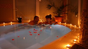 Una coppia in vasca idromassaggio con petali di rosa che galleggiano nell'acqua, circondati da candele.