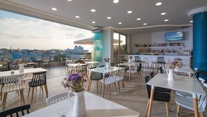 A rooftop restaurant with tables and chairs, a bar area, and a large TV screen. - Belvedere Village (Malevizi)