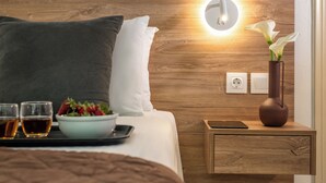 A neatly made bed with pillows, a bedside table with a vase of flowers, a tray with drinks and a bowl of fruit, and a wall-mounted light. - Belvedere Village (Malevizi)