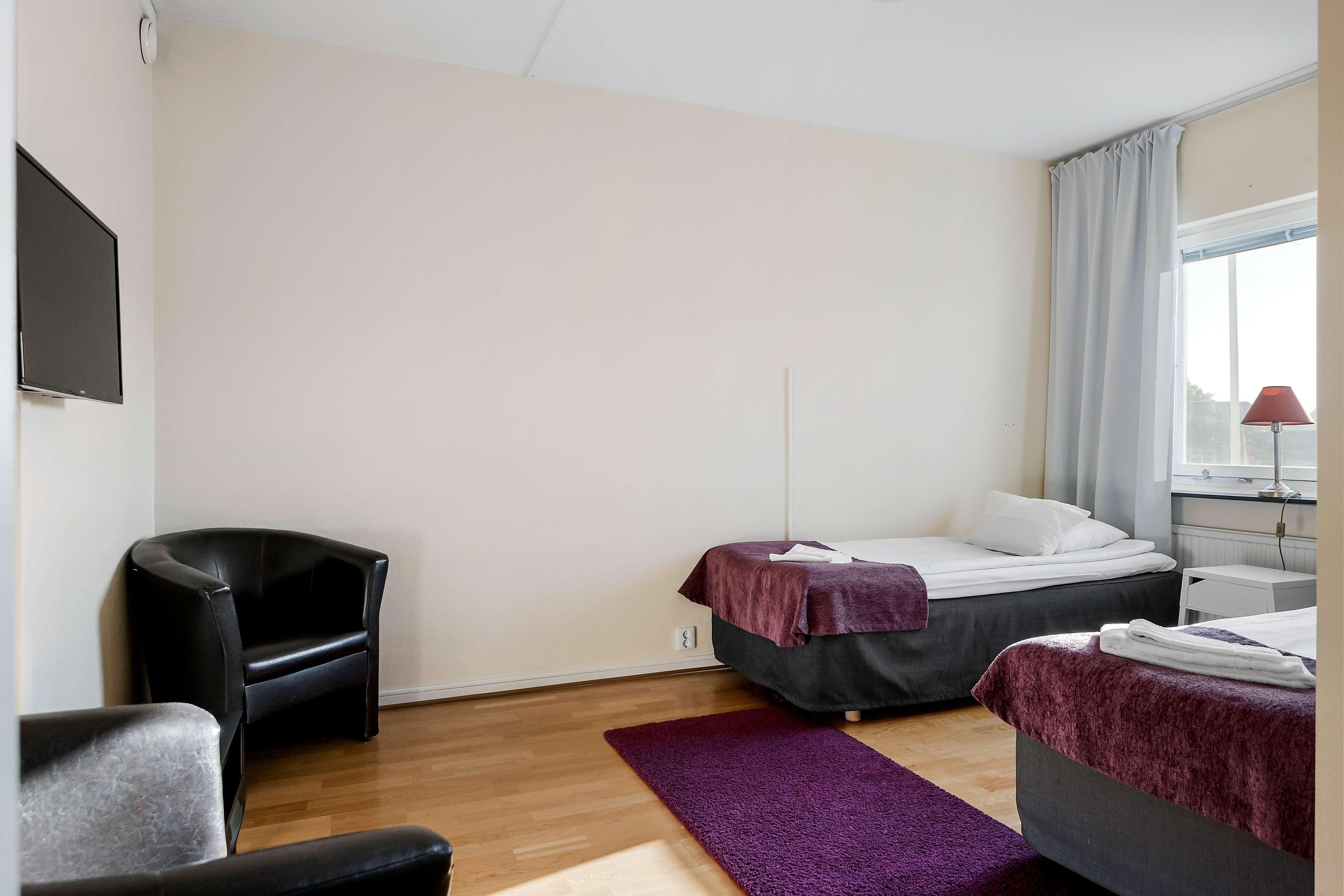 A room with two beds, a chair, a desk, and a TV.