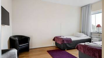 A room with two beds, a chair, a desk, and a TV.