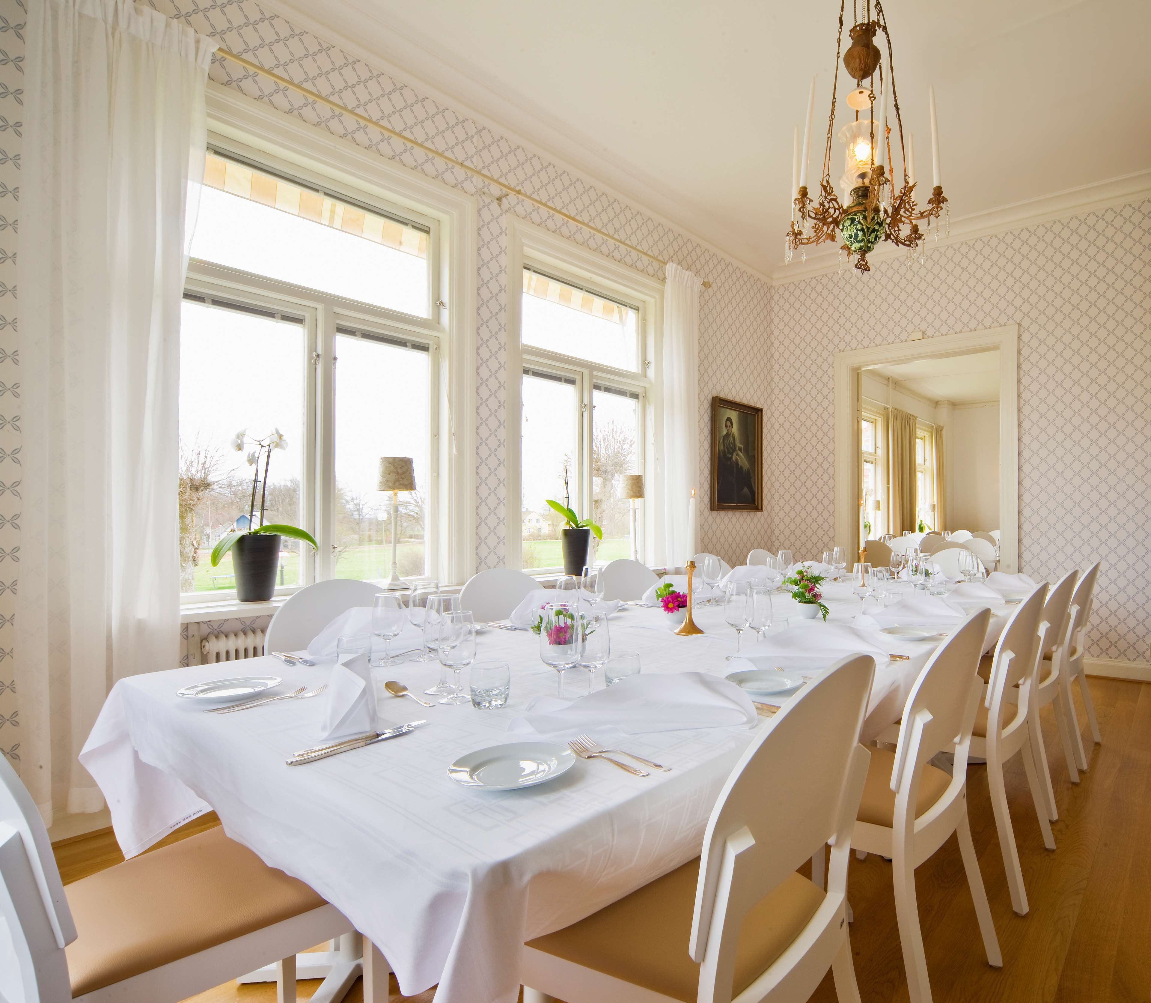 A dining room with a long table set for a meal, white chairs, and a chandelier.