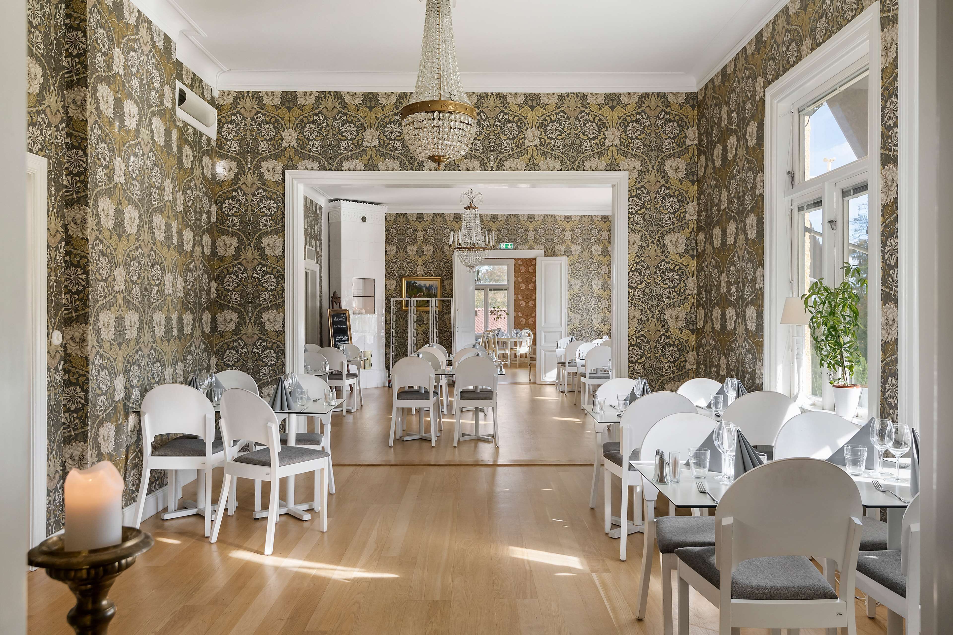 Un comedor con sillas y mesas blancas, una araña y un papel tapiz estampado.