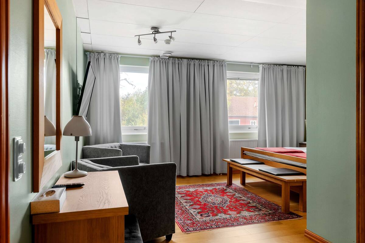 Een hotelkamer met een bed, een bureau, een stoel, een lamp en een rood vloerkleed.