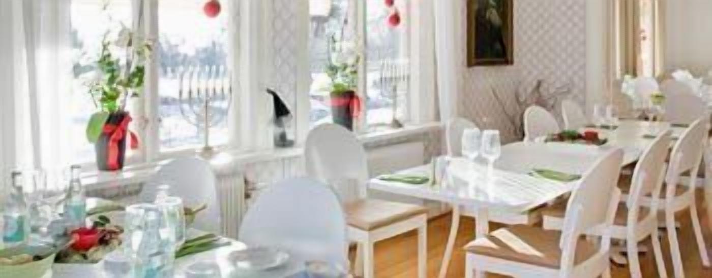 A dining area with white tables and chairs, potted plants, and a view of the outdoors.