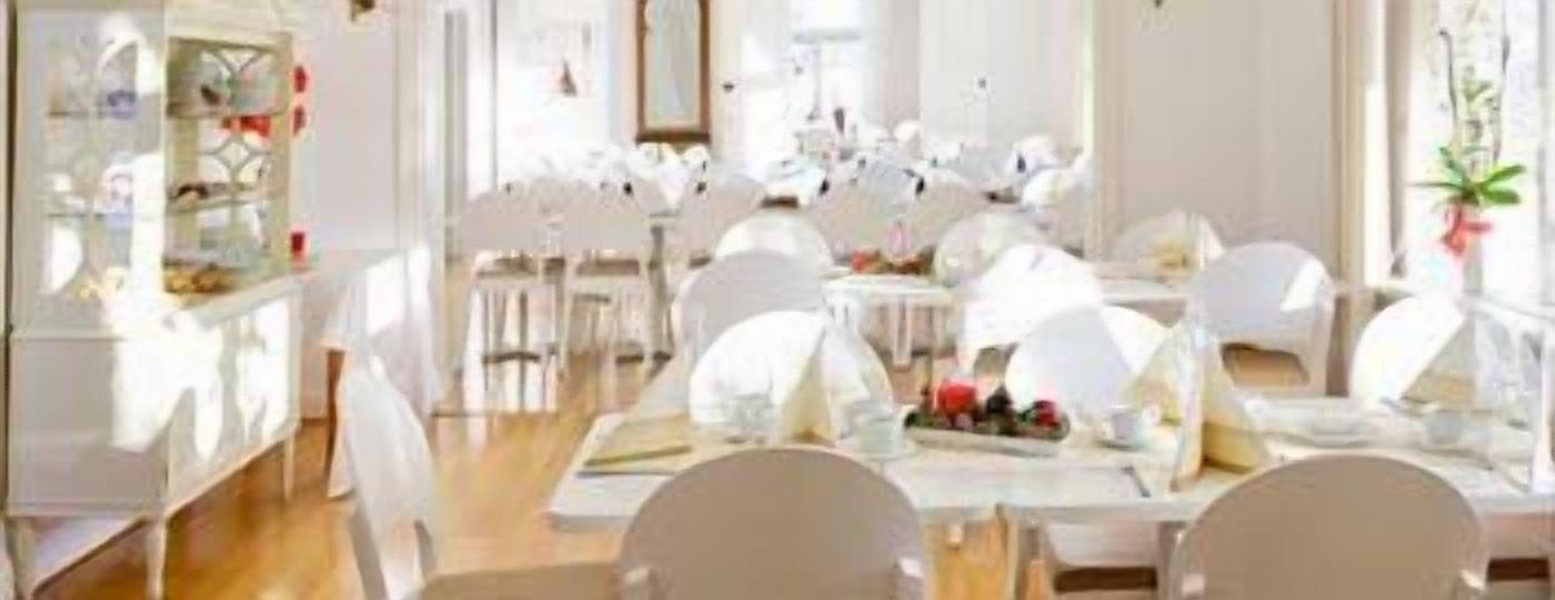 Een eetruimte met witte tafels en stoelen, een buffetopstelling en een helder, zonnig interieur.