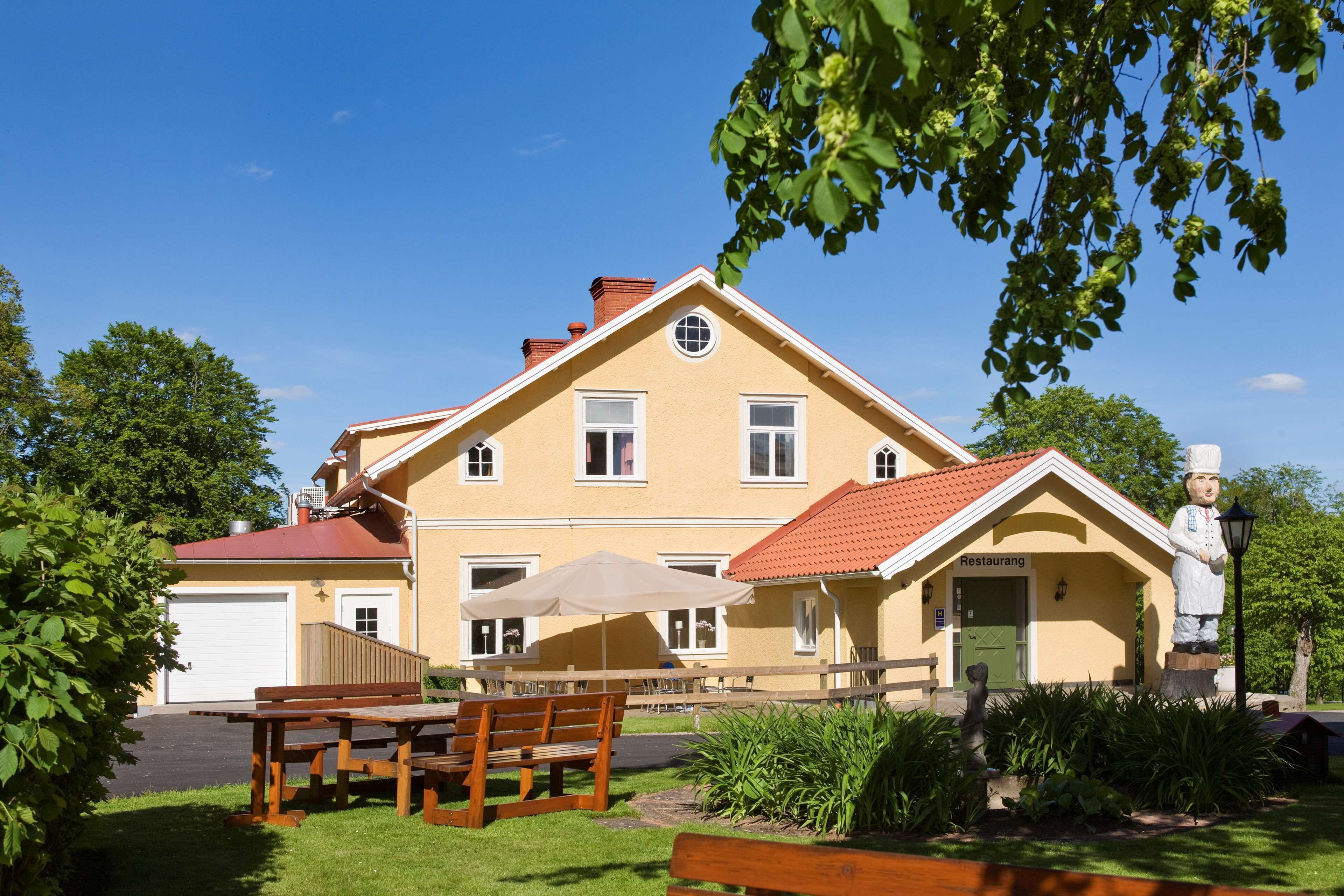 A two-story building with a red-tiled roof, a covered patio area with wooden benches, and a statue of a chef.