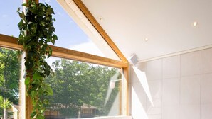 Un bain à remous avec vue sur les arbres et une maison, le tout visible à travers de grandes fenêtres.
