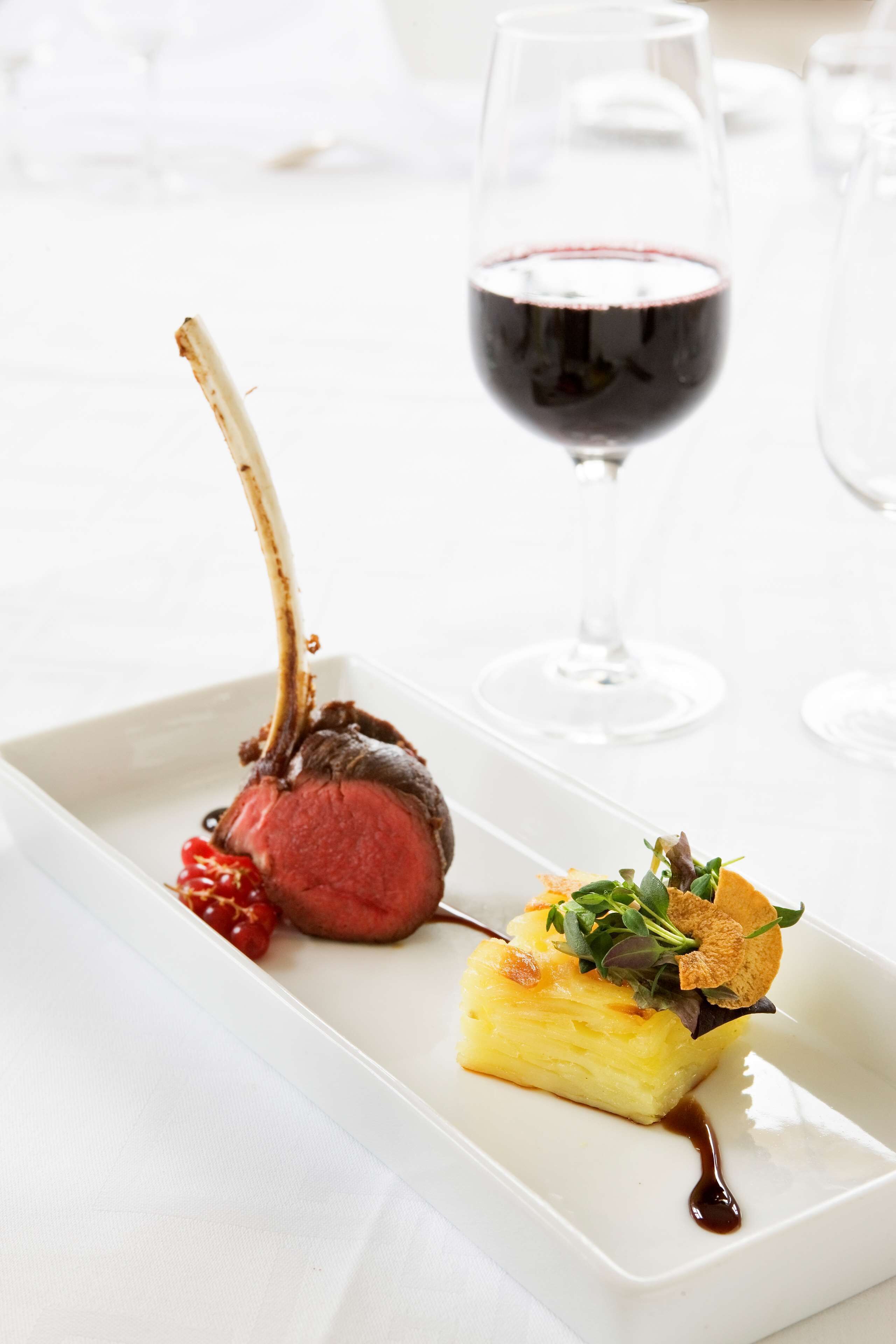 A white rectangular plate with a lamb chop, a slice of pineapple, and a small salad on a white tablecloth.