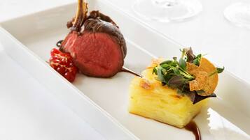 A white rectangular plate with a lamb chop, a slice of pineapple, and a small salad on a white tablecloth.
