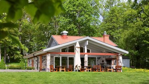 Un bâtiment à deux étages, doté d’une façade en pierre et d’un toit recouvert de tuiles rouges, comprenant un espace extérieur aménagé pour s’asseoir et une terrasse couverte.