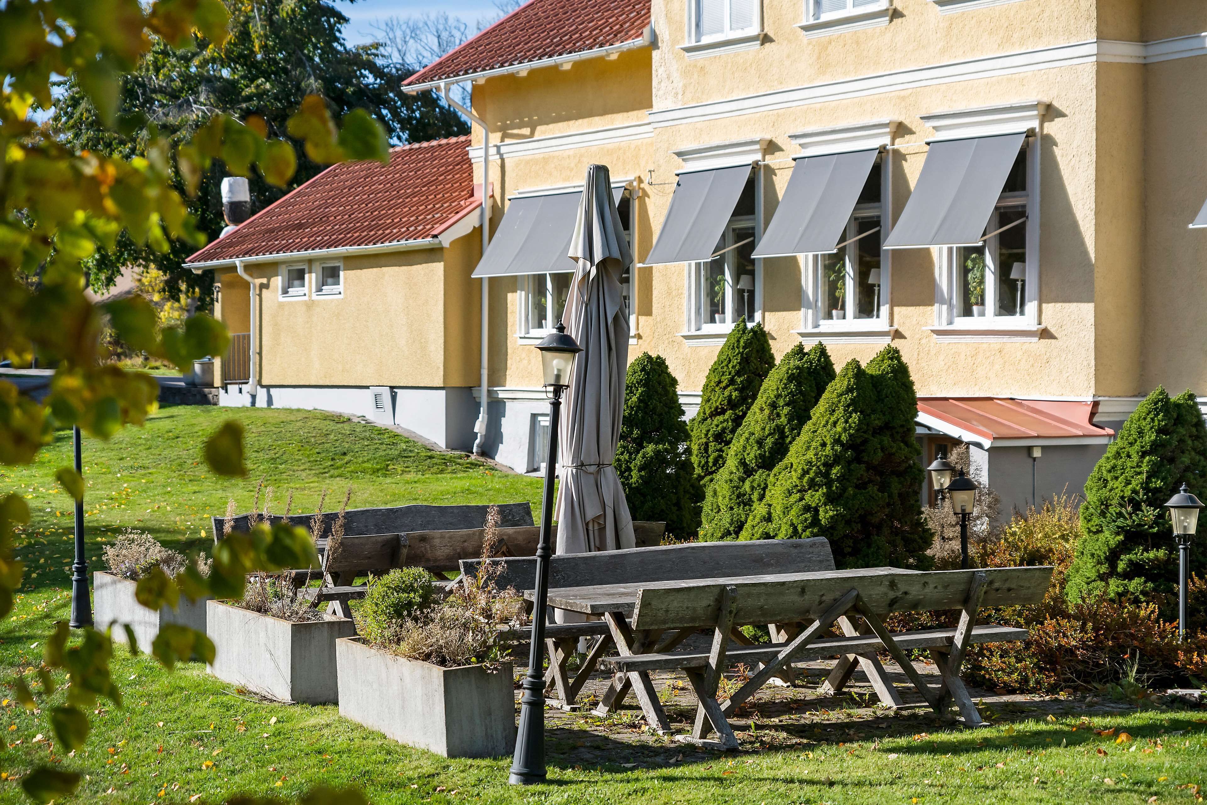 A yellow building with a red roof, outdoor seating, and a well-maintained garden.