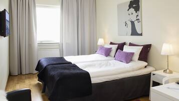 A hotel room with a bed, two bedside tables, a desk, a chair, a TV, and a window with curtains.