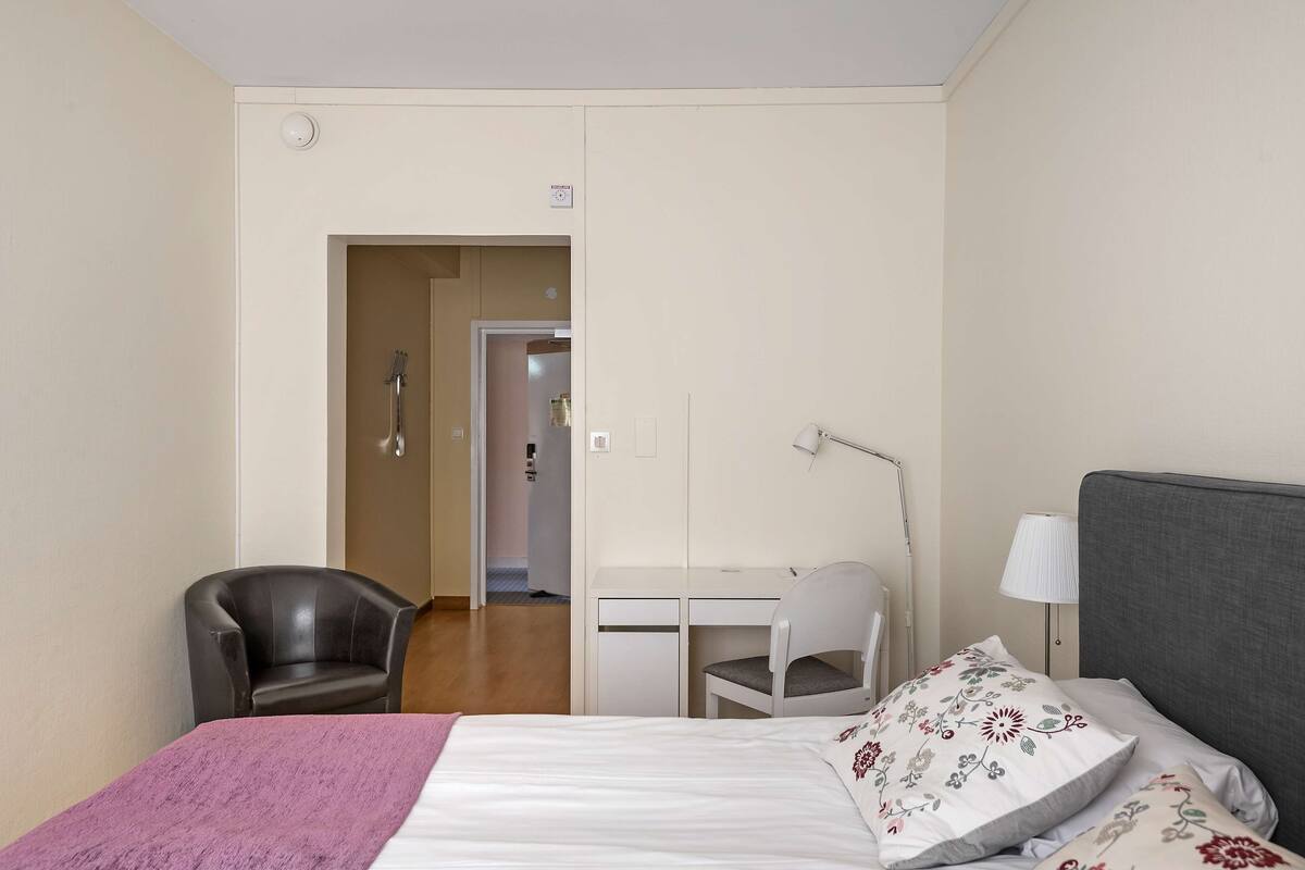 Een hotelkamer met een bed, een bureau, een stoel en een lamp.