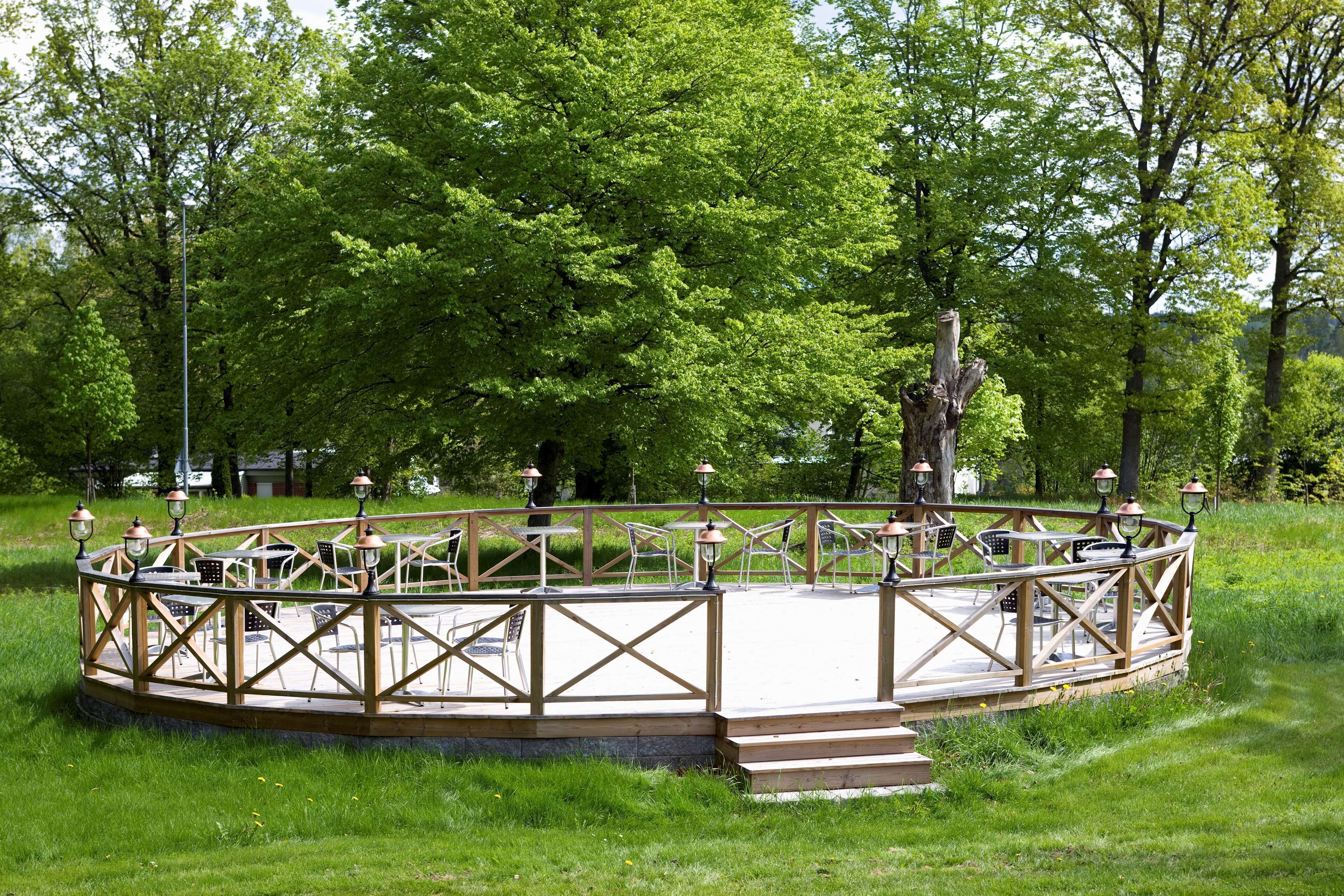 A circular wooden deck with outdoor seating and tables, surrounded by lush greenery.