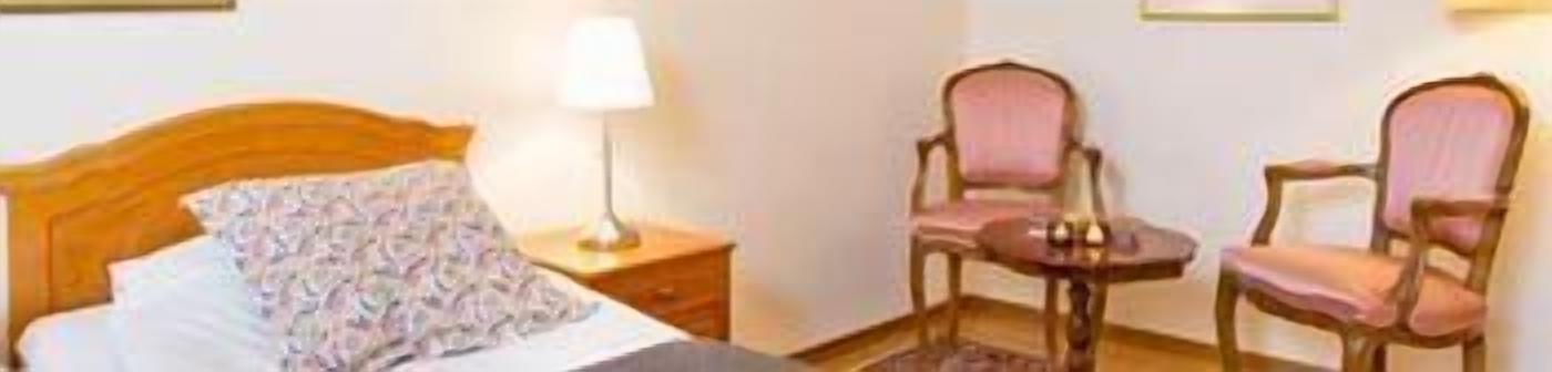 Ett hotellrum med en säng, ett nattduksbord med en lampa och två stolar.