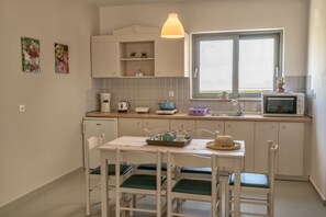 A kitchen with white cabinets, a window, a microwave, and a table with chairs. - Aloe Apartments & Studios (Rethymno)