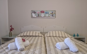 A double bed with striped bedding, two bedside tables with decorative items, and a wall-mounted artwork above the bed. - Aloe Apartments & Studios (Rethymno)