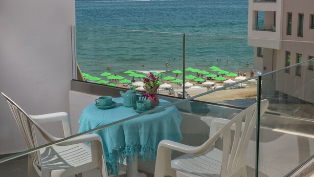 A balcony with a table set for two, overlooking a beach with umbrellas and people.