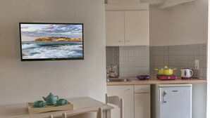 A small kitchen with a dining area, a refrigerator, a sink, and a television displaying a scenic view.