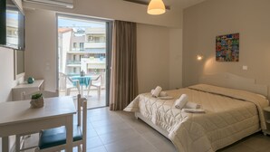 A hotel room with a bed, a desk, a chair, a dining table, a balcony, and a view of the outside buildings.