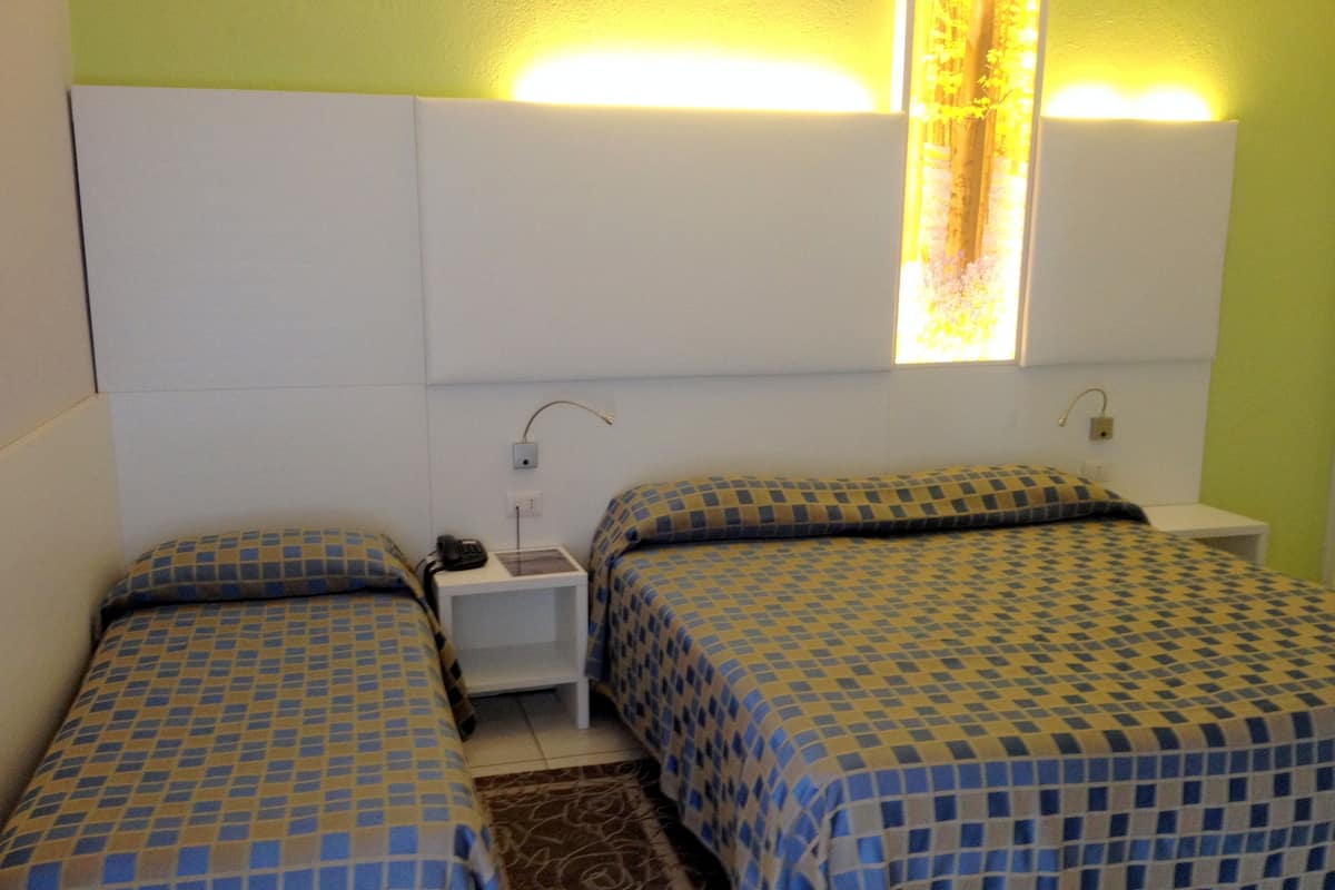 Una habitación con dos camas, cada una con colcha a cuadros, una mesita de noche con lámpara y una ventana con cortinas.