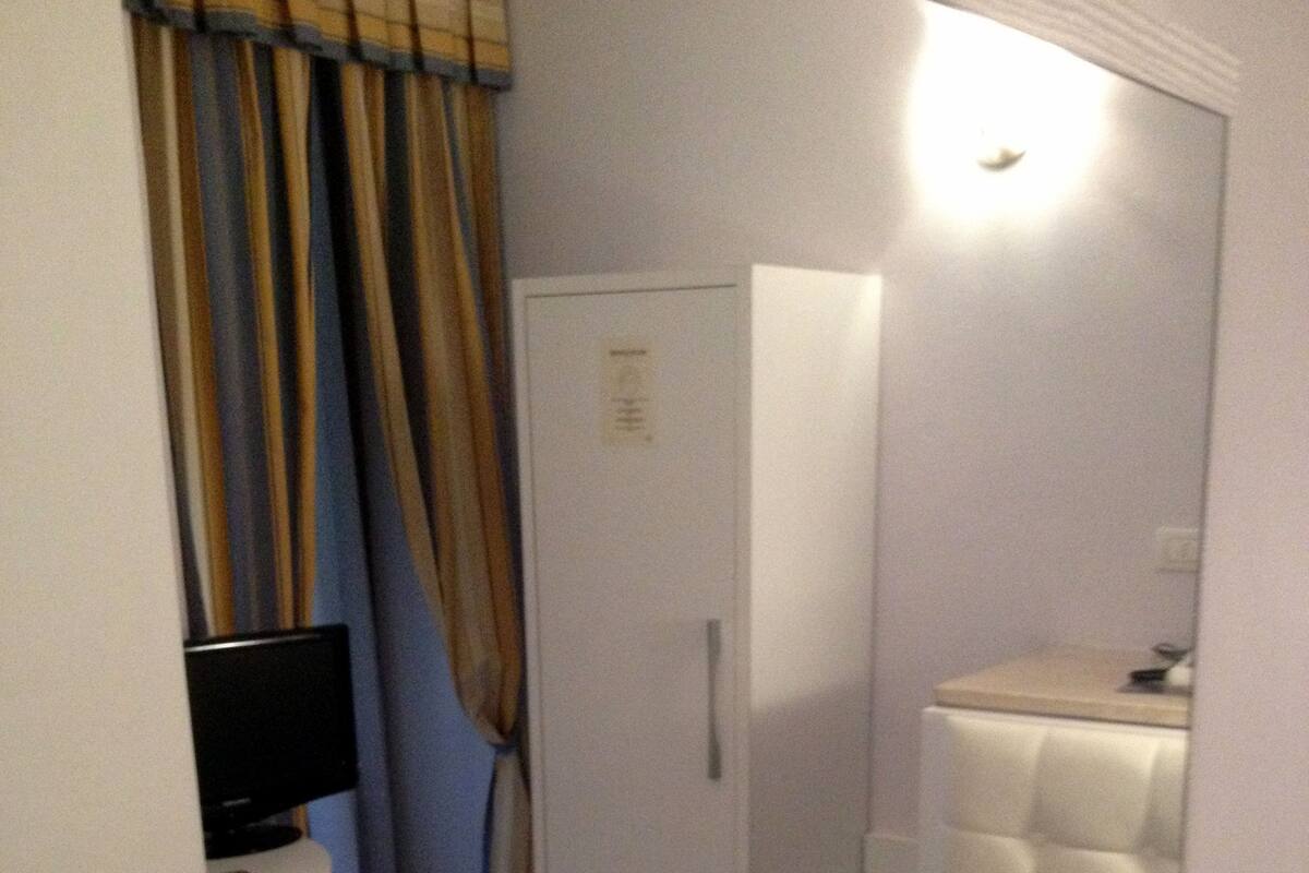Una habitación pequeña y estrecha con cama, televisor, armario y baño.