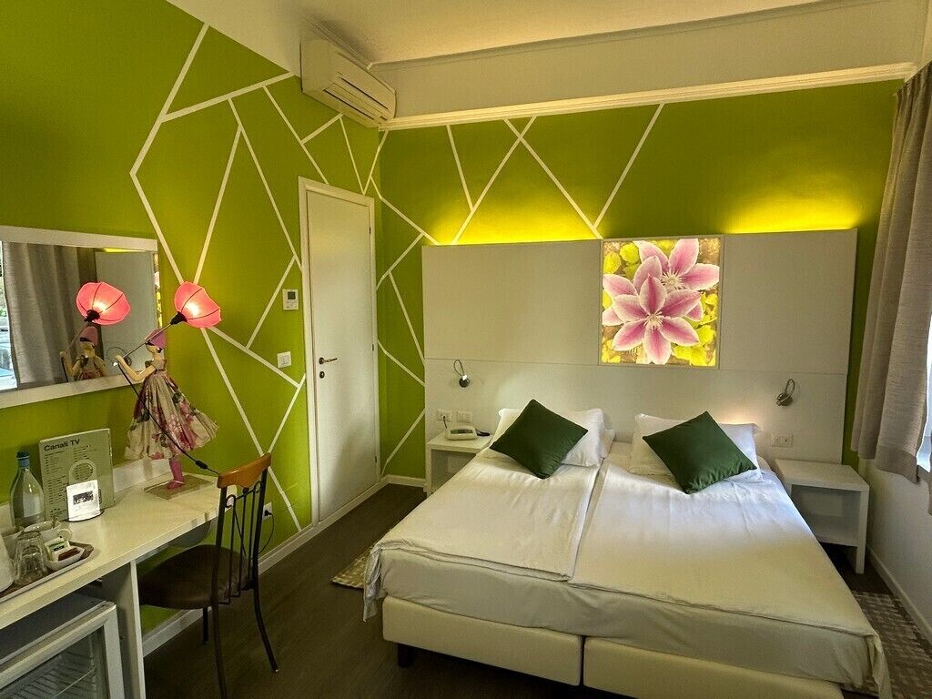 A hotel room with a bed, a desk, a chair, a TV, and a painting on the wall.