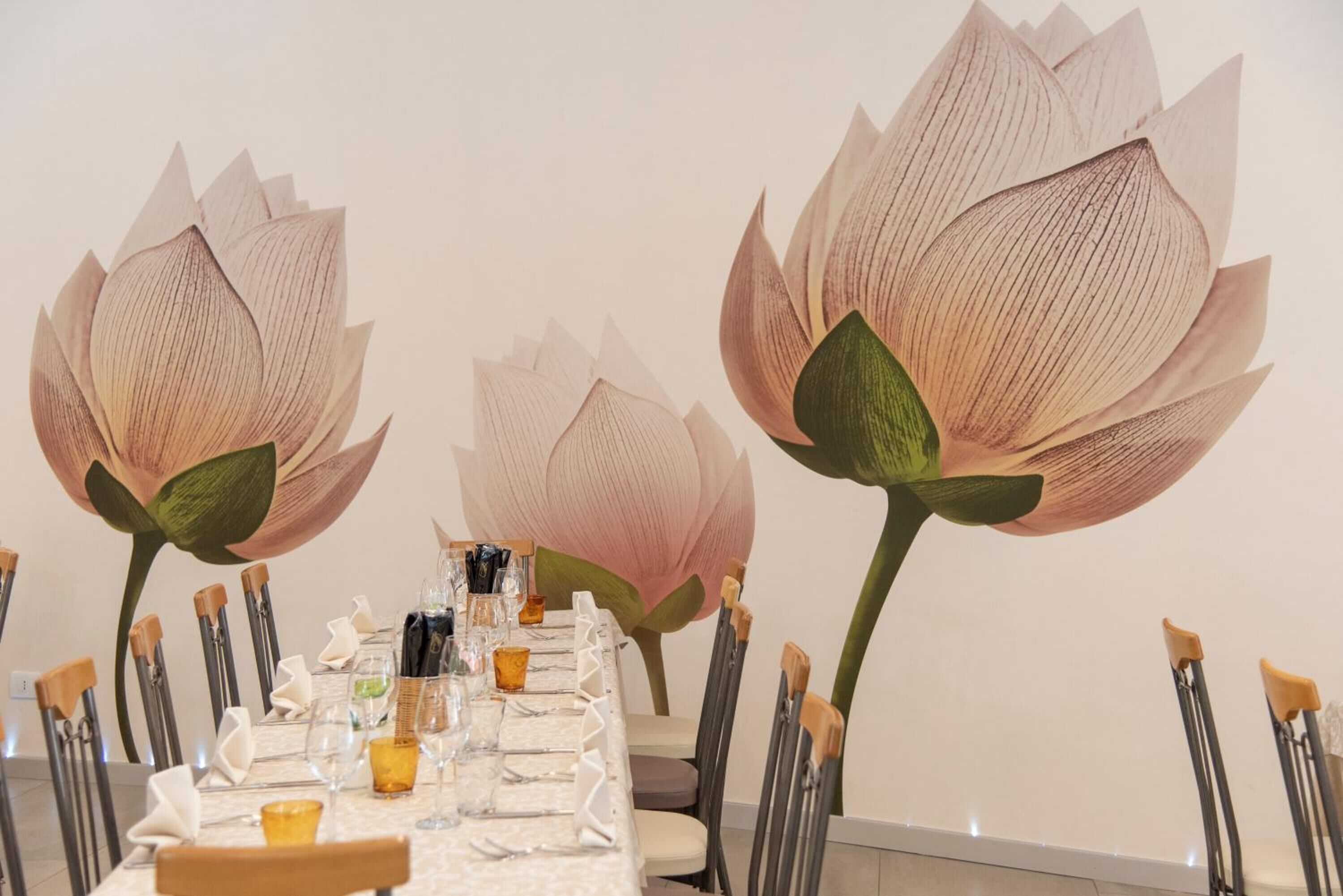 Een eettafel gedekt met stoelen, glazen en een decoratieve muurdecoratie van lotusbloemen.