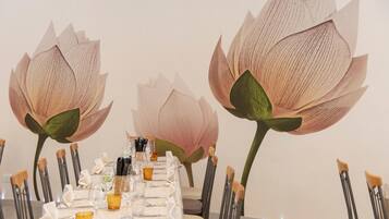 Een eettafel gedekt met stoelen, glazen en een decoratieve muurdecoratie van lotusbloemen.