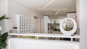 Un área de recepción con un mostrador blanco, un espejo grande y un estante en la pared con varios objetos.