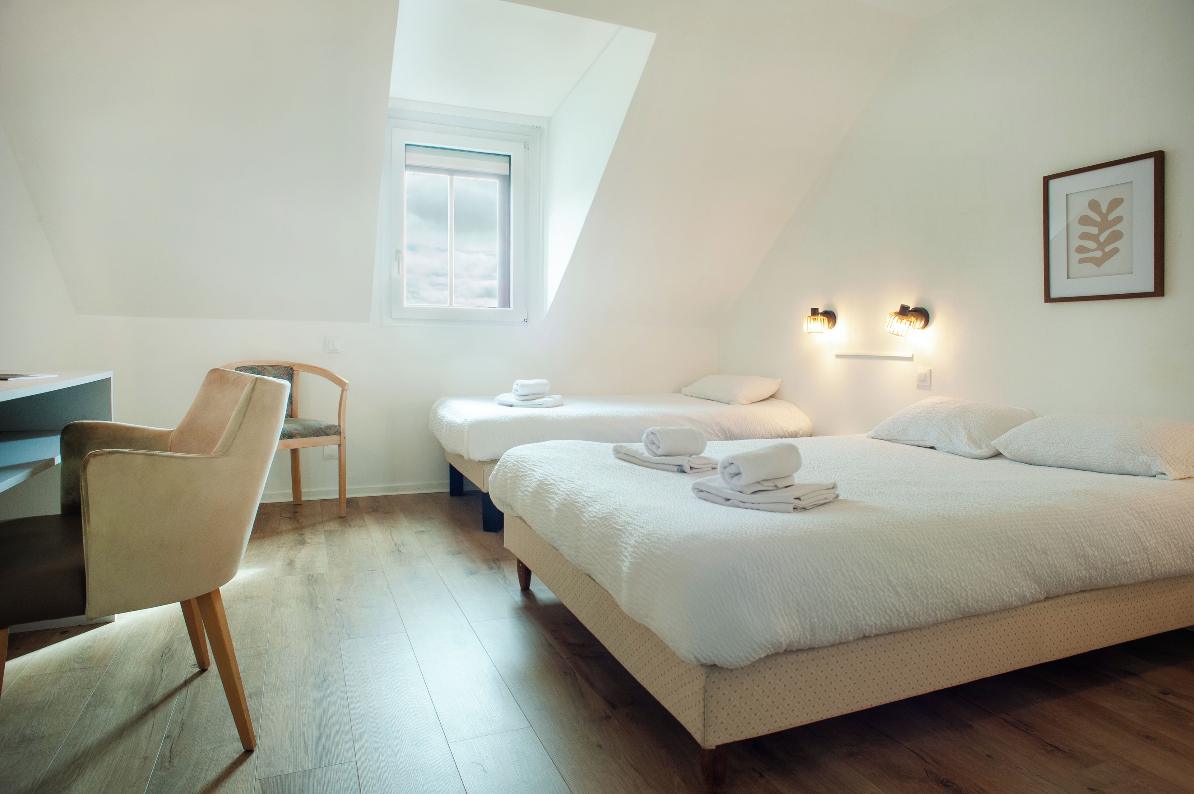 Ein Schlafzimmer mit Schreibtisch, zwei Betten, einem Sessel und einem Fenster.