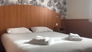 Una habitación de hotel con cabecera de madera, cama con sábanas blancas y una mesita de noche de madera.