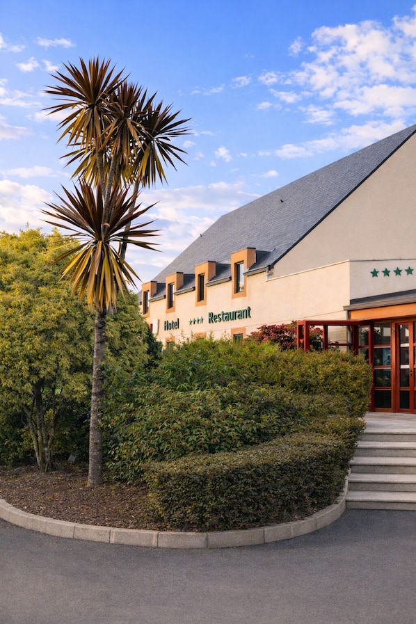 A hotel with a restaurant, a palm tree, and a clear sky. - Logis Hôtel Restaurant Les Fontaines (Lanvollon)