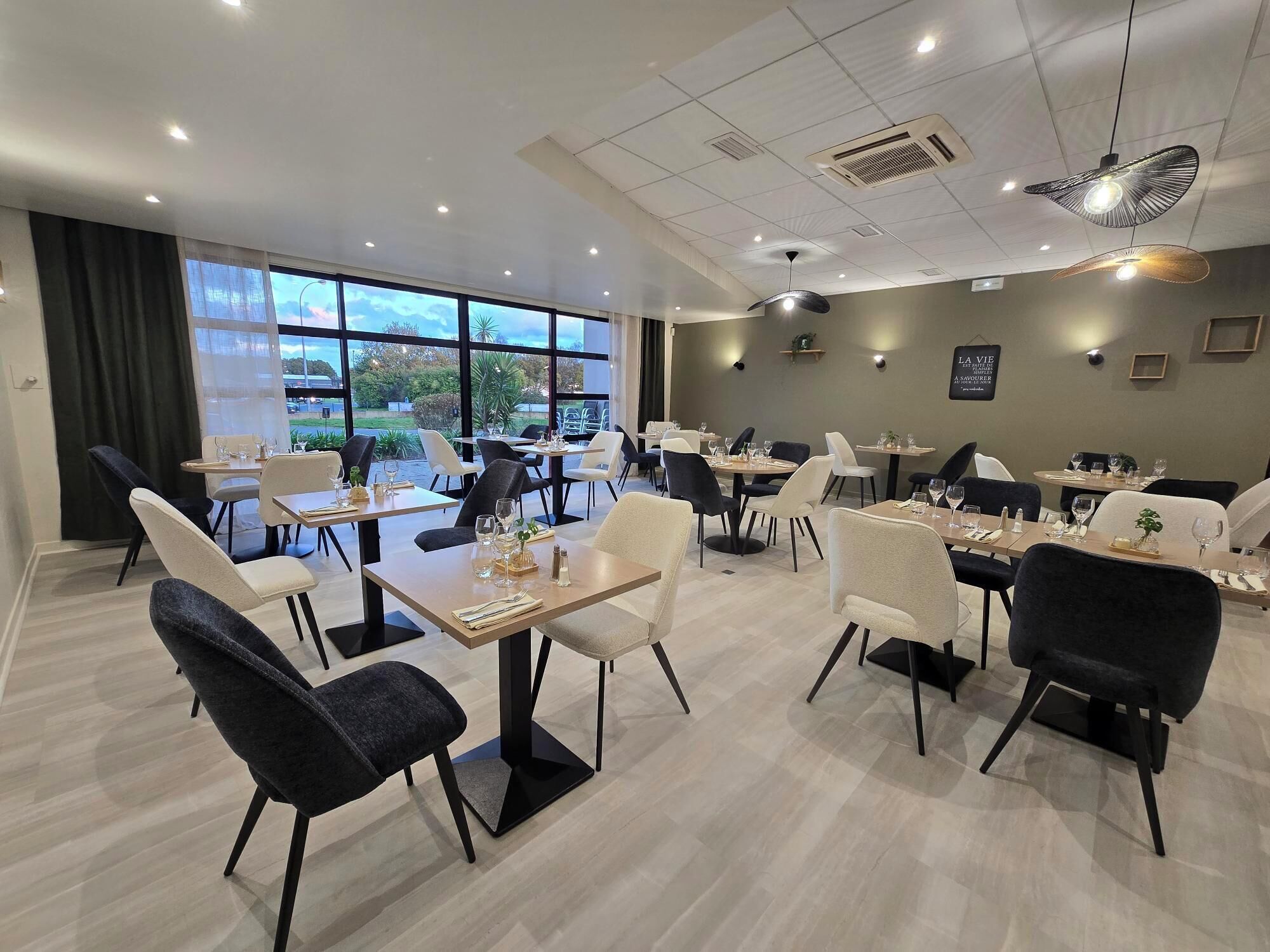 Un comedor moderno con mesas, sillas, ventanas amplias e iluminación de techo.