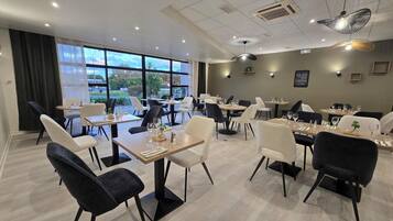 Un comedor moderno con mesas, sillas, ventanas amplias e iluminación de techo.