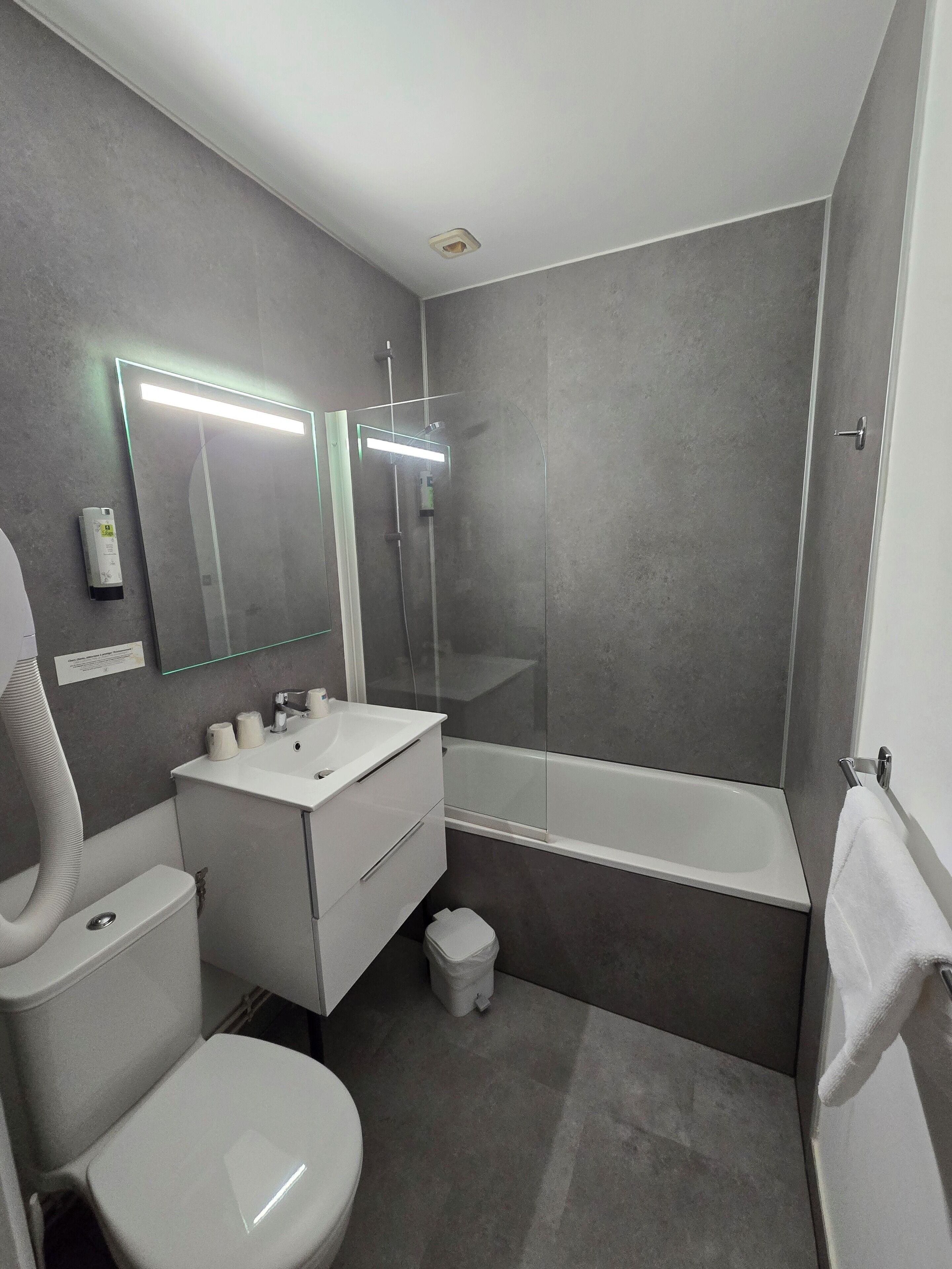 A modern bathroom with a toilet, sink, mirror, and bathtub.