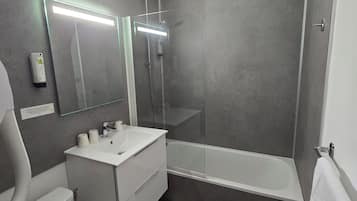 A modern bathroom with a toilet, sink, mirror, and bathtub.