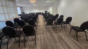 Un salón de conferencias con filas de sillas, una mesa central y una lámpara colgante.