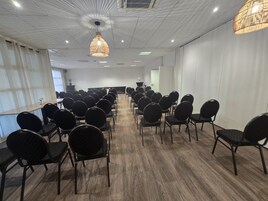 Uma sala de conferências com fileiras de cadeiras, uma mesa central e um lustre.