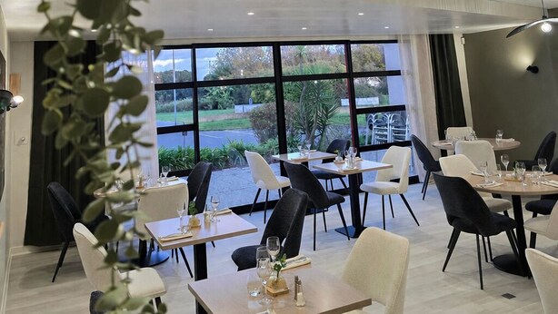 Un restaurante moderno con mesas y sillas, ventanas amplias y plantas de interior.