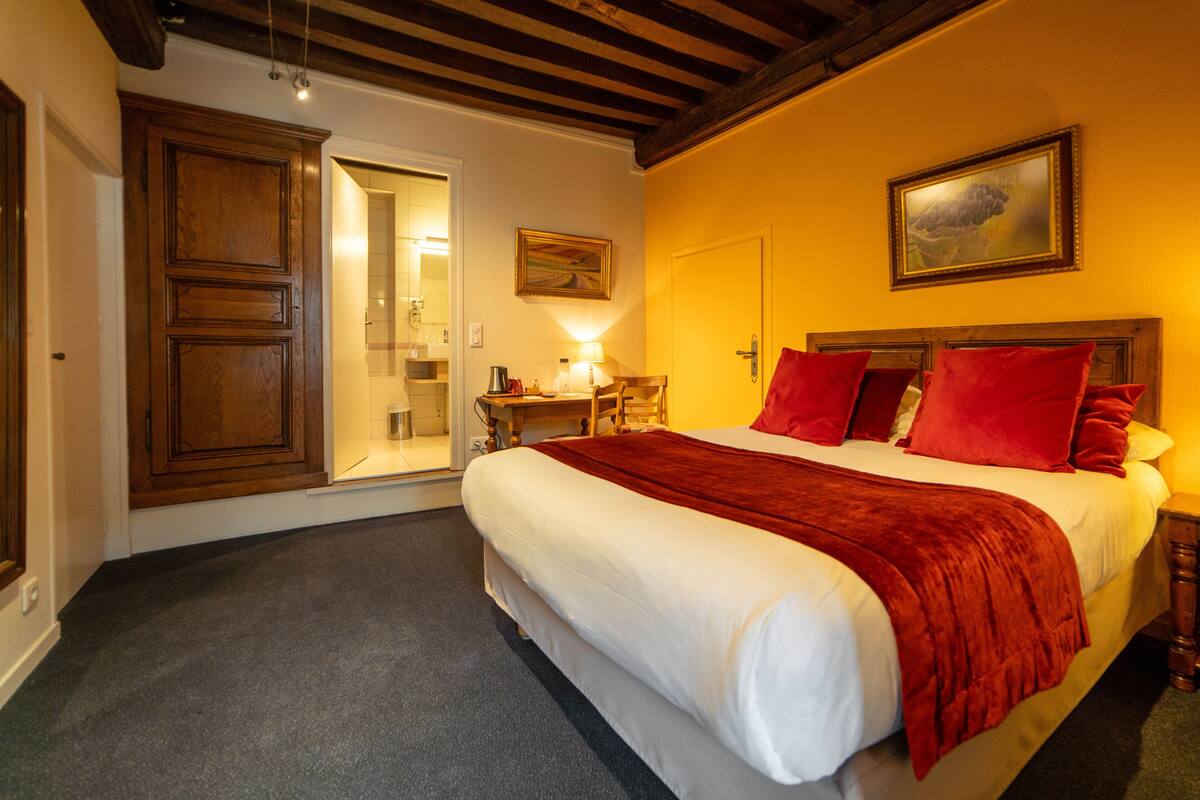 Un dormitorio con una cama grande, un armario de madera, un escritorio con una silla y un cuadro en la pared.