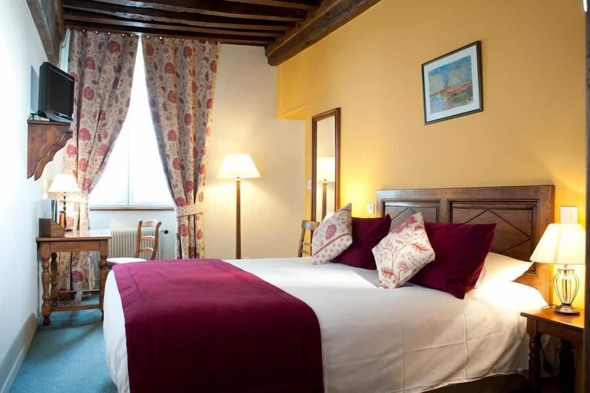 Habitación de hotel con cama, dos lámparas de noche, televisor, escritorio con silla y ventana con cortinas.